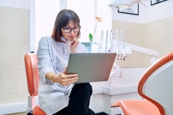 Dentist reviewing year-end paperwork on a laptop in her private dental practice